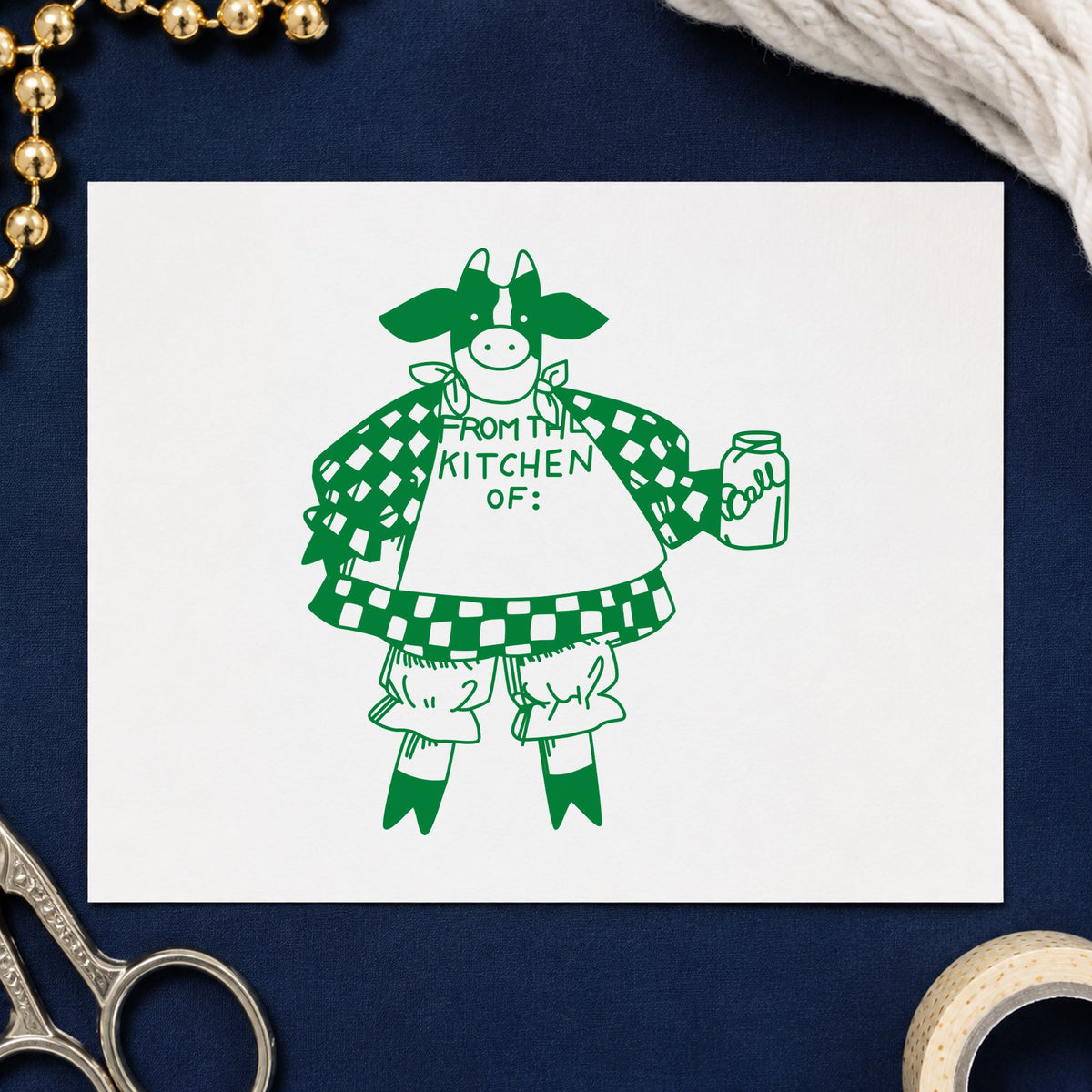 From the Kitchen Of Cow Rubber Stamp impression in green ink on white paper in a styled craft setting.