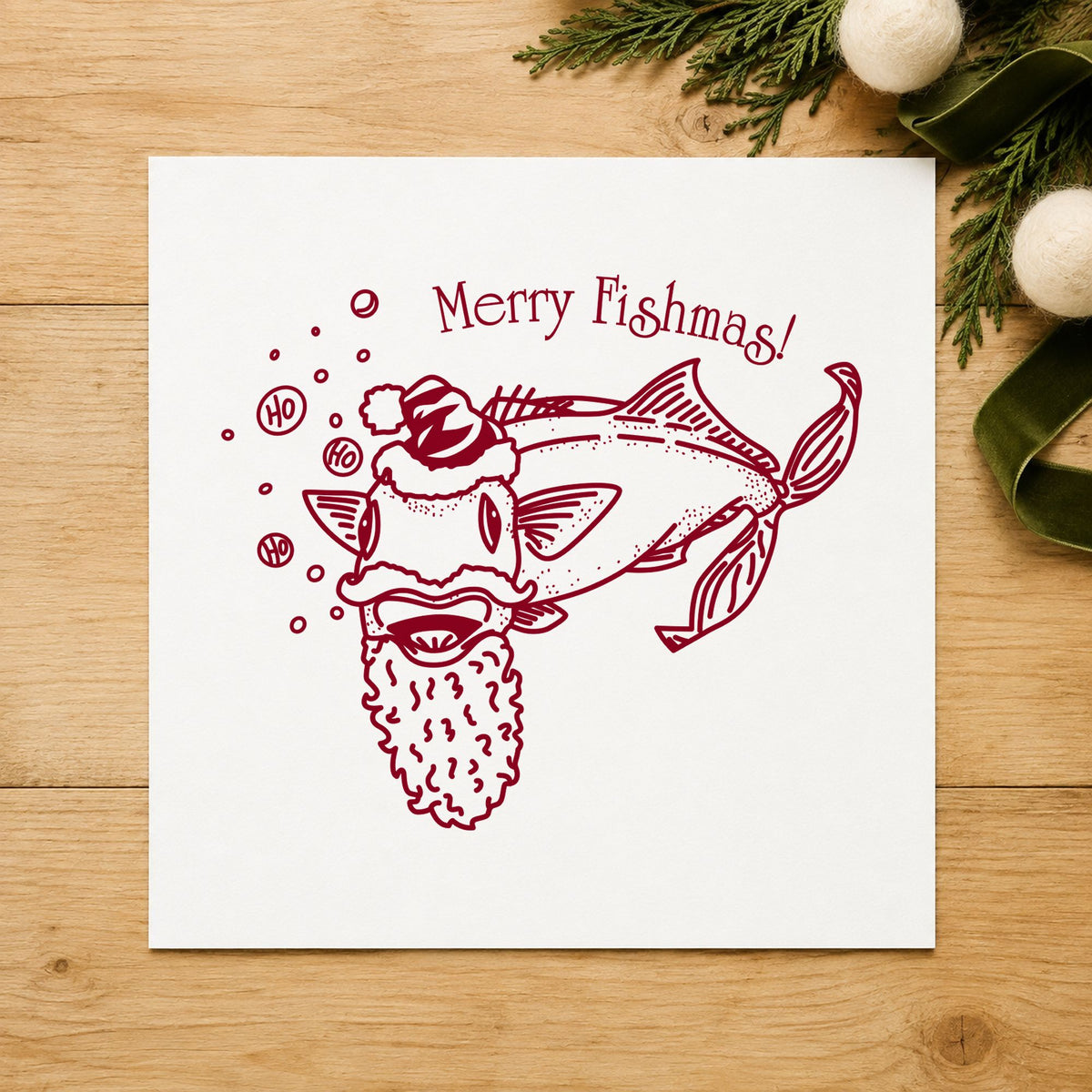 Merry Fishmas Catfish Rubber Stamp impression in burgundy ink on white paper in a styled craft setting.