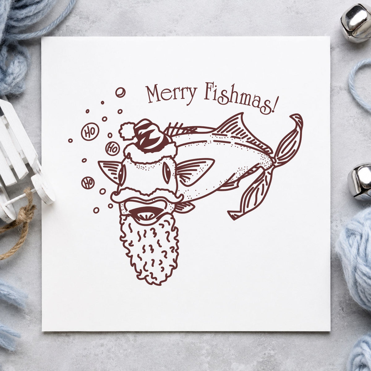 Merry Fishmas Catfish Rubber Stamp impression in brown ink on white paper in a styled craft setting.