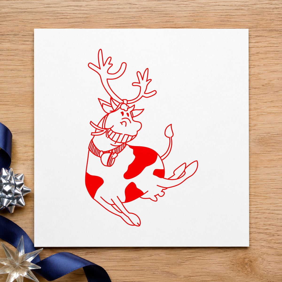 Leaping Cow with Reindeer Antlers Rubber Stamp impression in red ink on white paper in a styled craft setting.