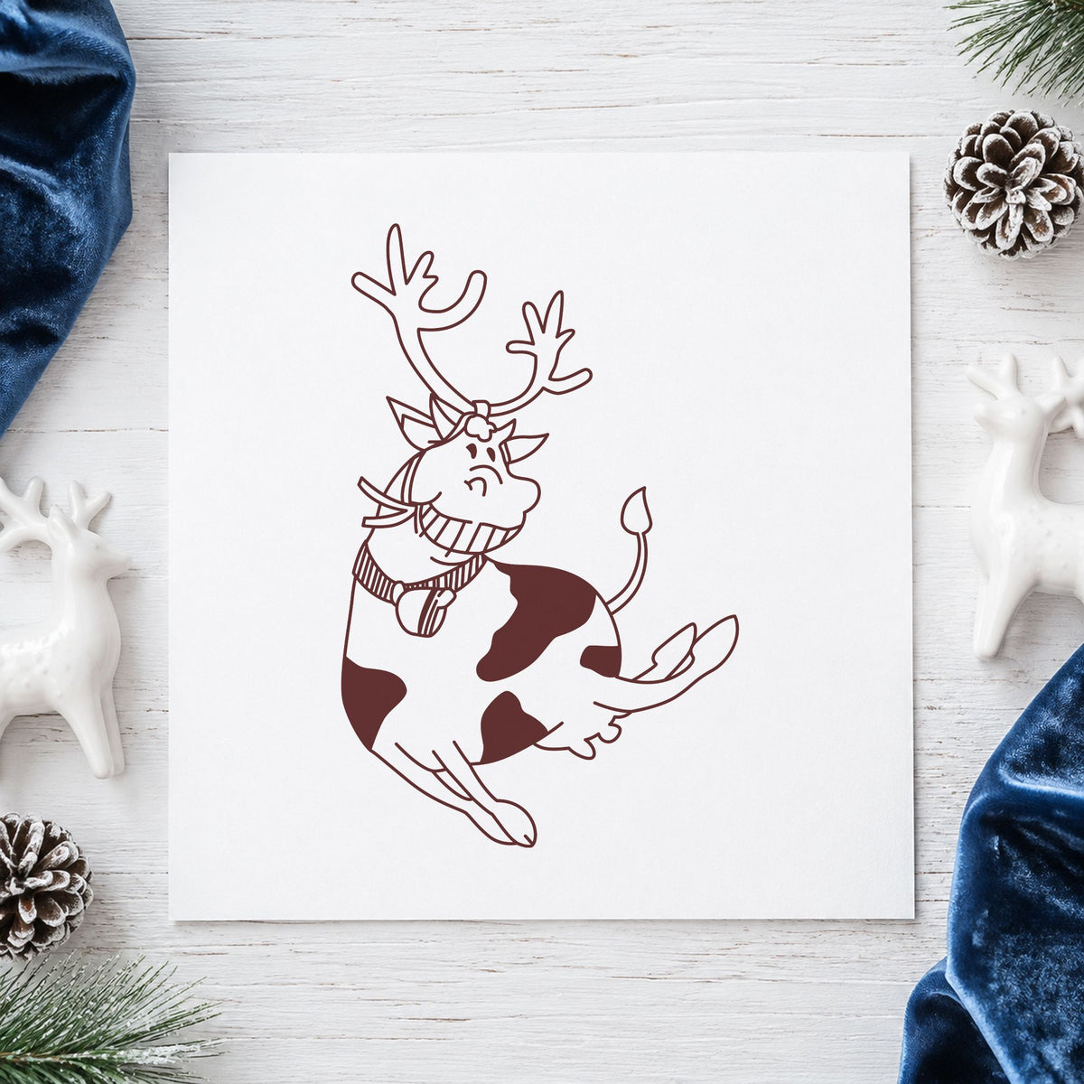 Leaping Cow with Reindeer Antlers Rubber Stamp impression in brown ink on white paper in a styled craft setting.