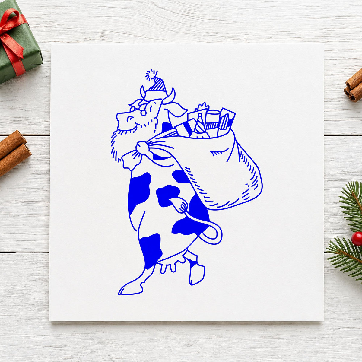 Santa Cow with Gift Sack Rubber Stamp Large impression in blue ink on white paper in a styled craft setting.