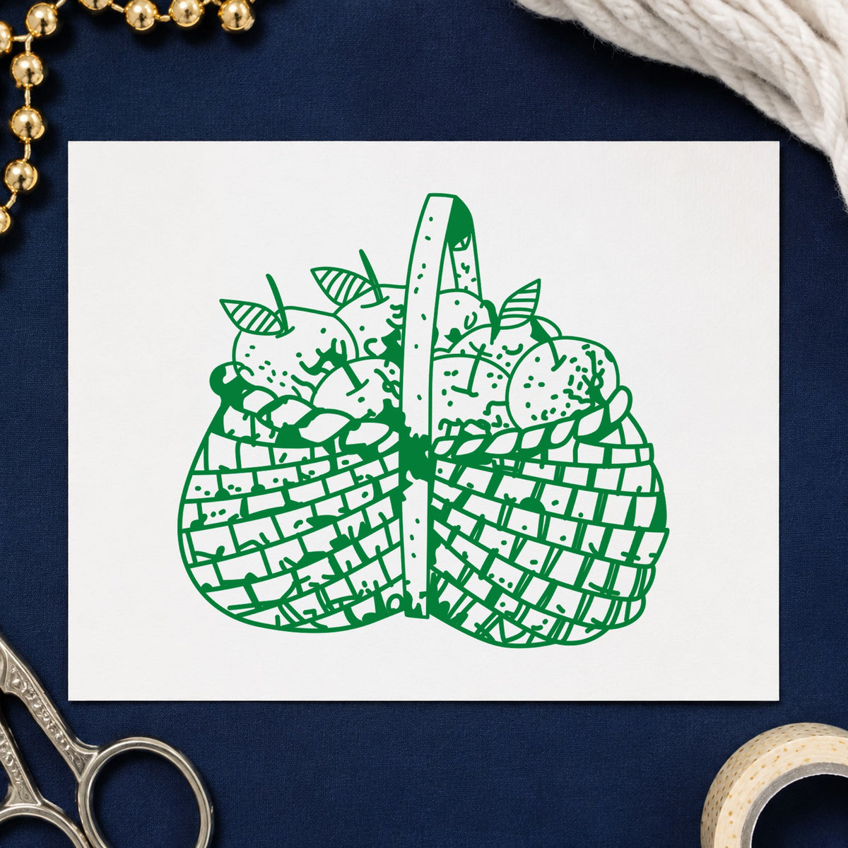 Basket Brimming with Apples Rubber Stamp impression in green ink on white paper in a styled craft setting.