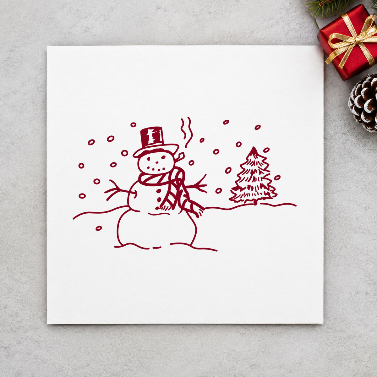 Snowman in Winter Landscape Rubber Stamp impression in burgundy ink on white paper in a styled craft setting.