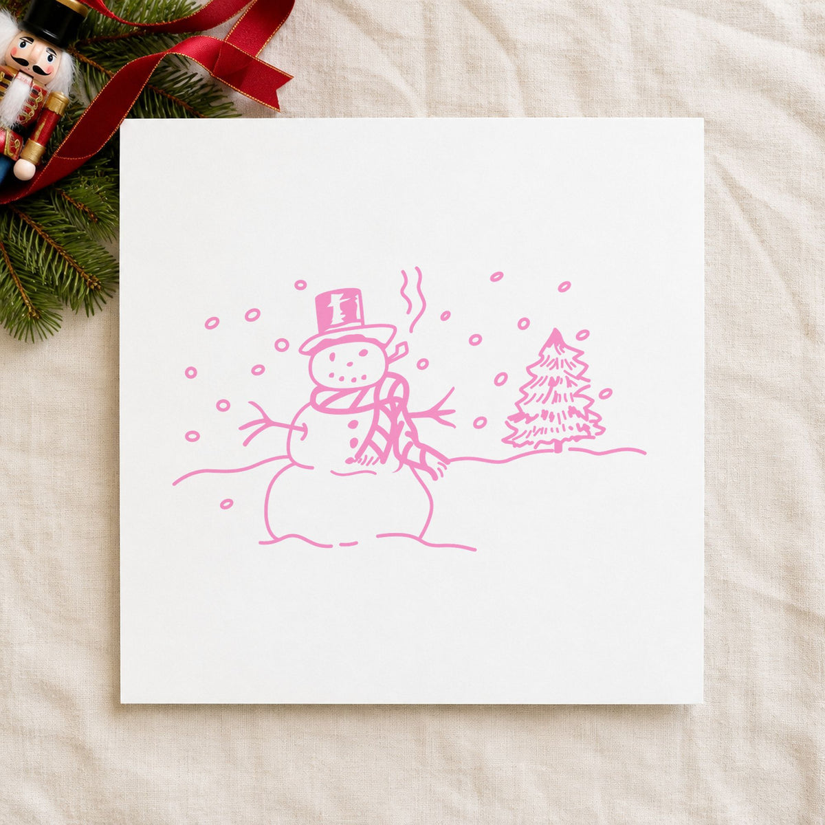 Snowman in Winter Landscape Rubber Stamp impression in pink ink on white paper in a styled craft setting.