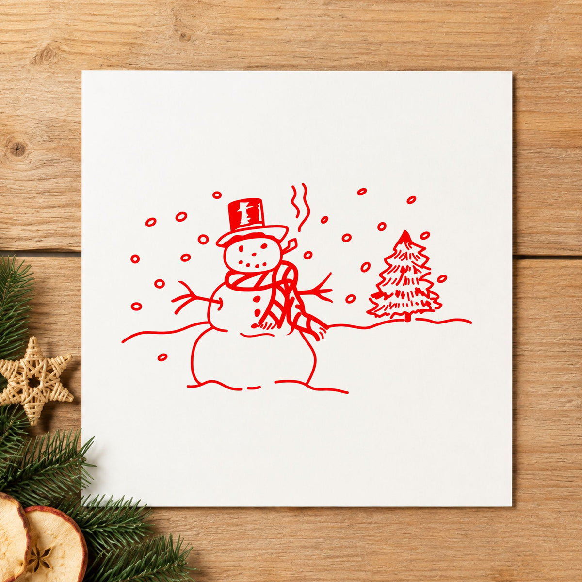 Snowman in Winter Landscape Rubber Stamp impression in red ink on white paper in a styled craft setting.