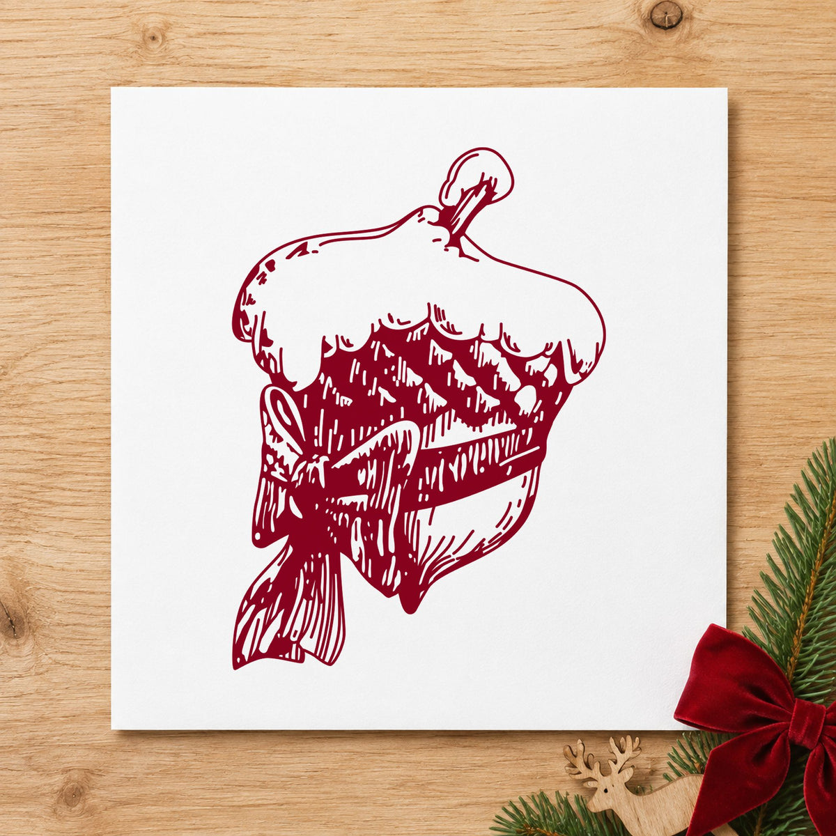 Snowy Acorn with Bow Christmas Rubber Stamp impression in burgundy ink on white paper in a styled craft setting.