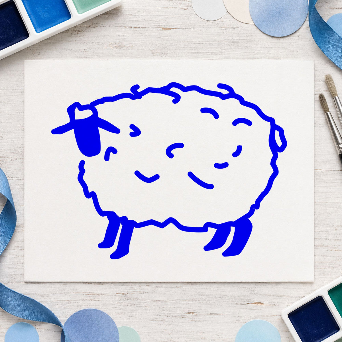 Folk Art Sheep Rubber Stamp impression in blue ink on white paper in a styled craft setting.