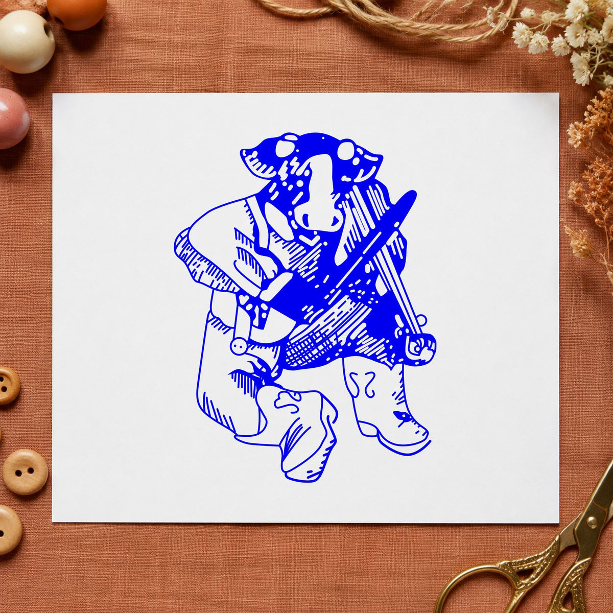 Fiddle Playing Cow Rubber Stamp impression in blue ink on white paper in a styled craft setting.