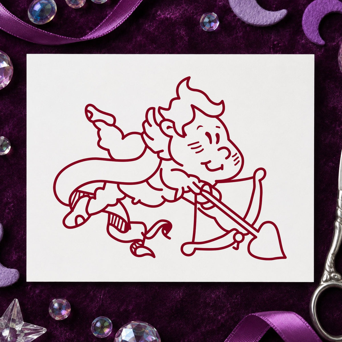 Cupid Shooting Heart Arrow Rubber Stamp impression in burgundy ink on white paper in a styled craft setting.