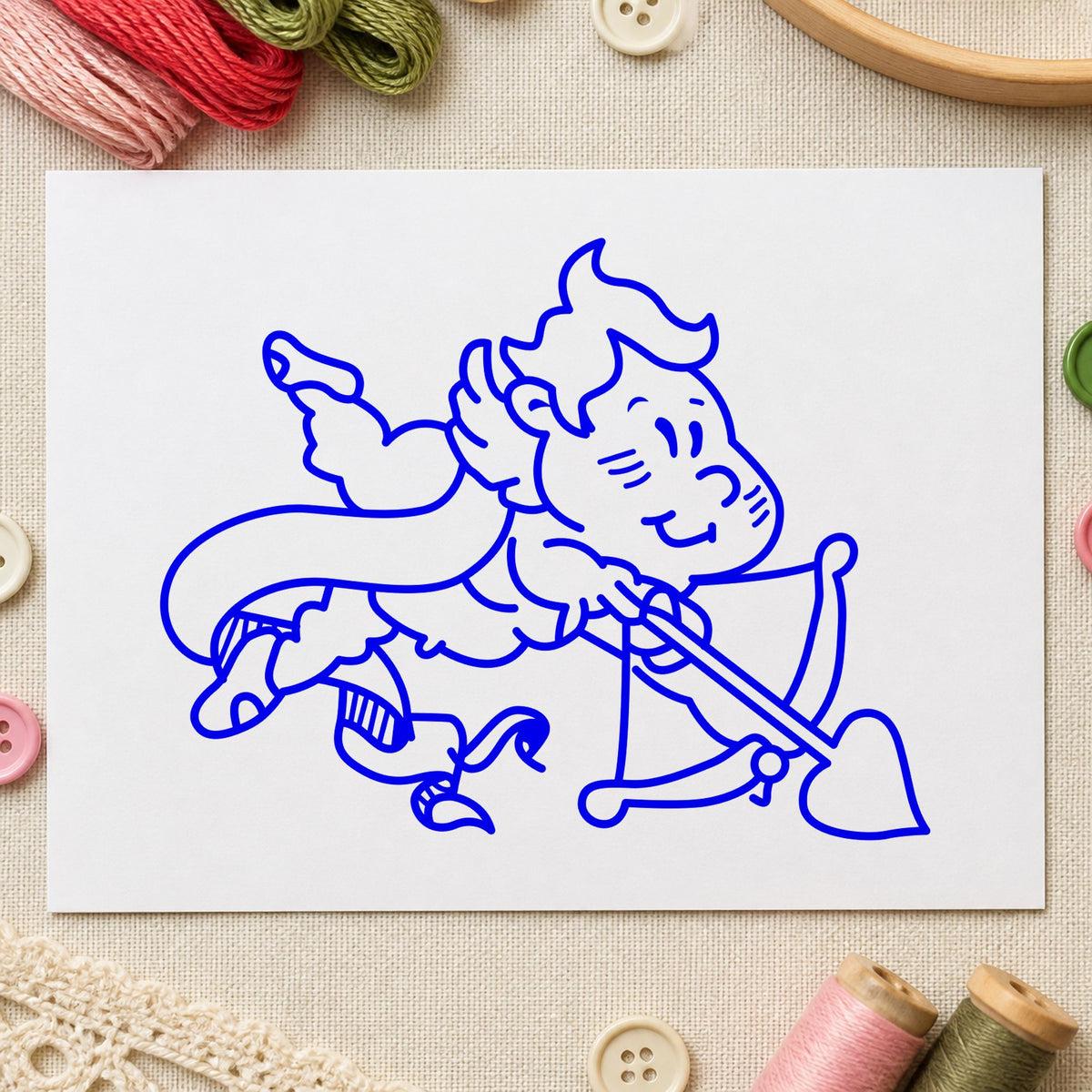 Cupid Shooting Heart Arrow Rubber Stamp impression in blue ink on white paper in a styled craft setting.