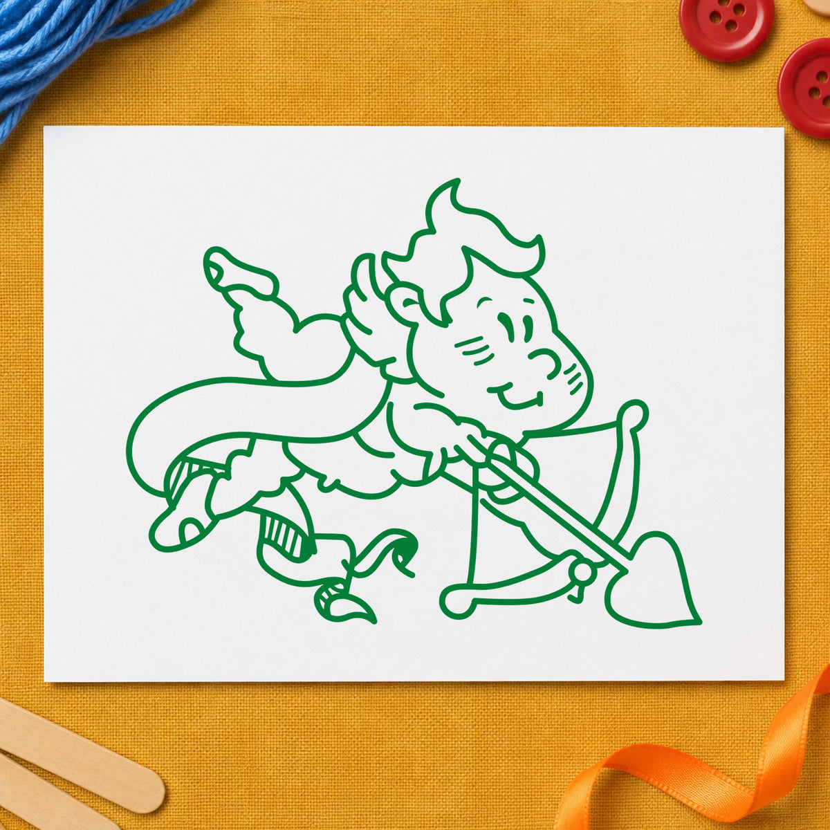 Cupid Shooting Heart Arrow Rubber Stamp impression in green ink on white paper in a styled craft setting.