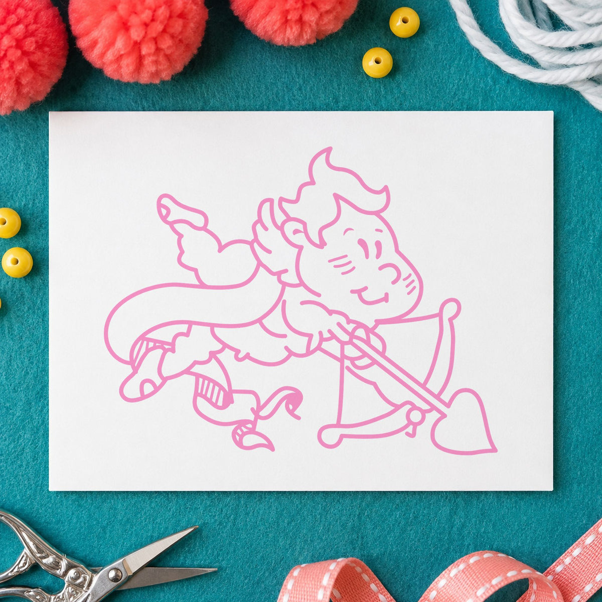 Cupid Shooting Heart Arrow Rubber Stamp impression in pink ink on white paper in a styled craft setting.