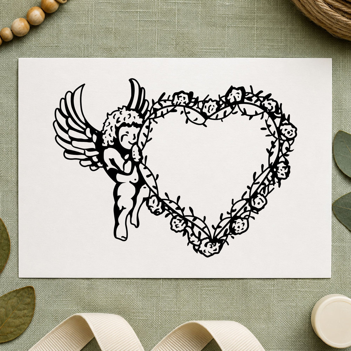 Cupid Holding Vine Heart Rubber Stamp impression in black ink on white paper in a styled craft setting.