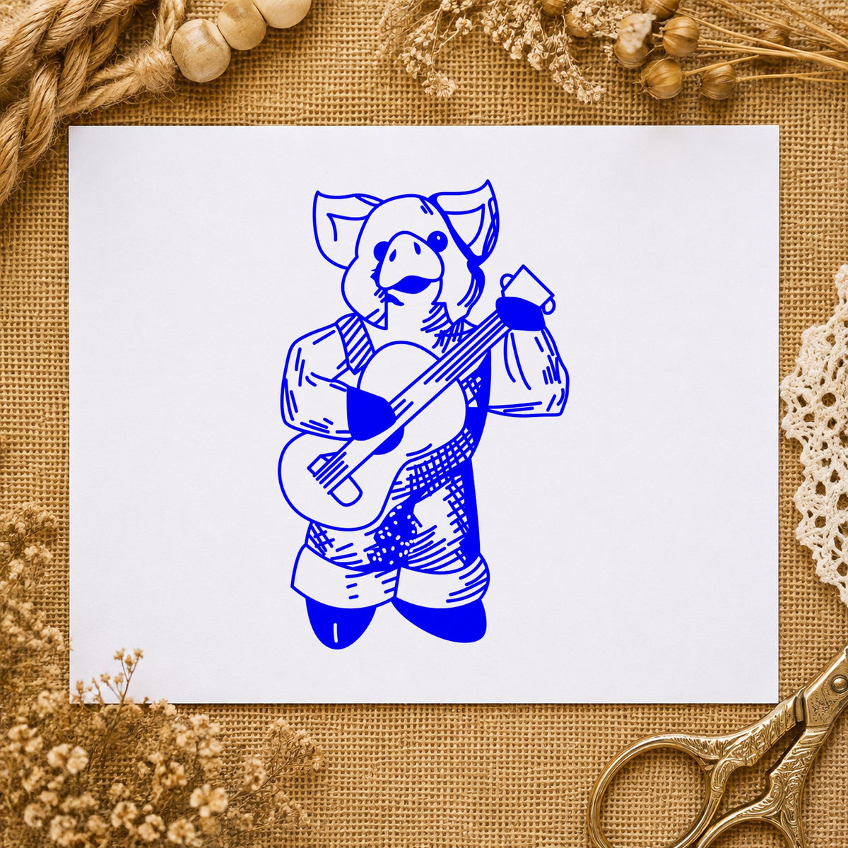 Banjo Playing Pig Rubber Stamp impression in blue ink on white paper in a styled craft setting.