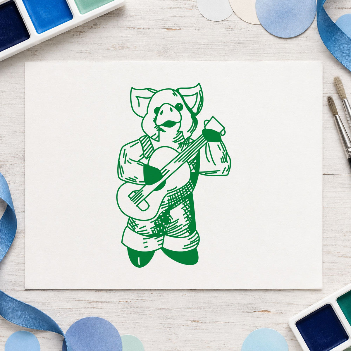 Banjo Playing Pig Rubber Stamp impression in green ink on white paper in a styled craft setting.