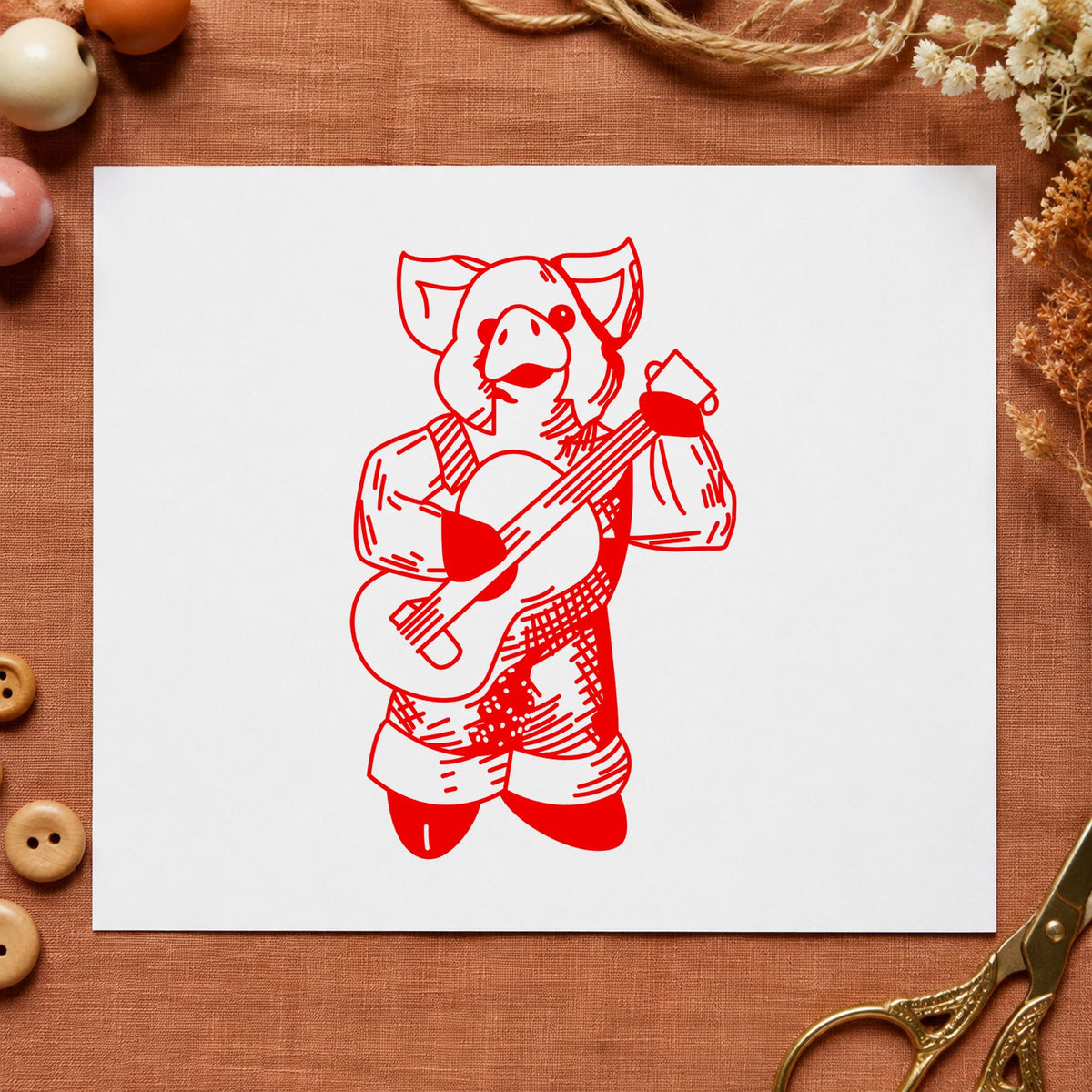 Banjo Playing Pig Rubber Stamp impression in red ink on white paper in a styled craft setting.