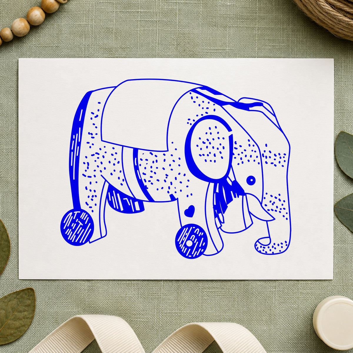 Wheeled Elephant Toy Rubber Stamp impression in blue ink on white paper in a styled craft setting.