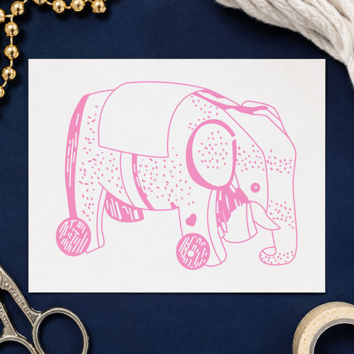 Wheeled Elephant Toy Rubber Stamp impression in pink ink on white paper in a styled craft setting.