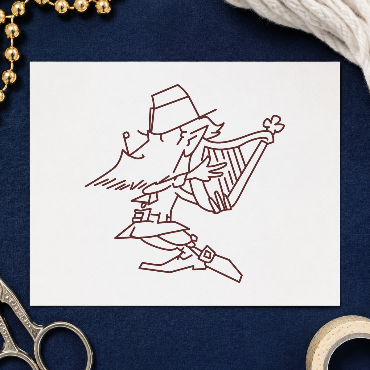 Leprechaun Playing Harp Rubber Stamp impression in brown ink on white paper in a styled craft setting.