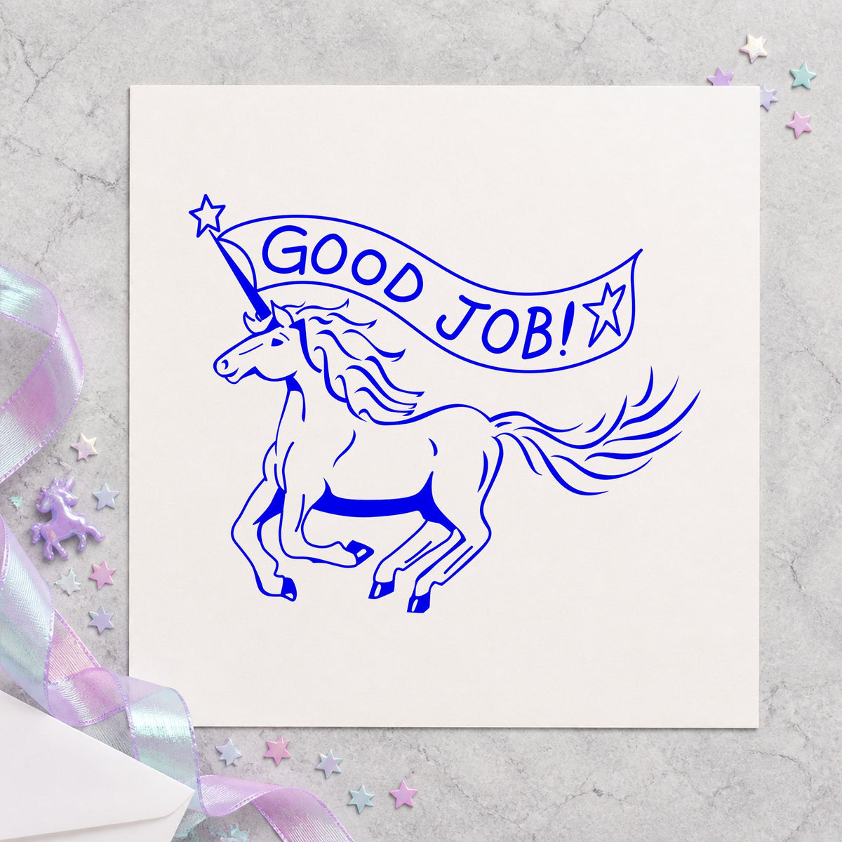Good Job Unicorn Rubber Stamp impression in blue ink on white paper in a styled craft setting.