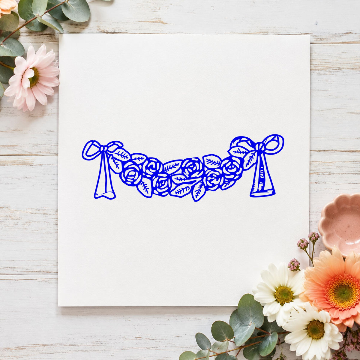 Blue wedding invitation stamp impression featuring the rose swag with bows design on white paper.