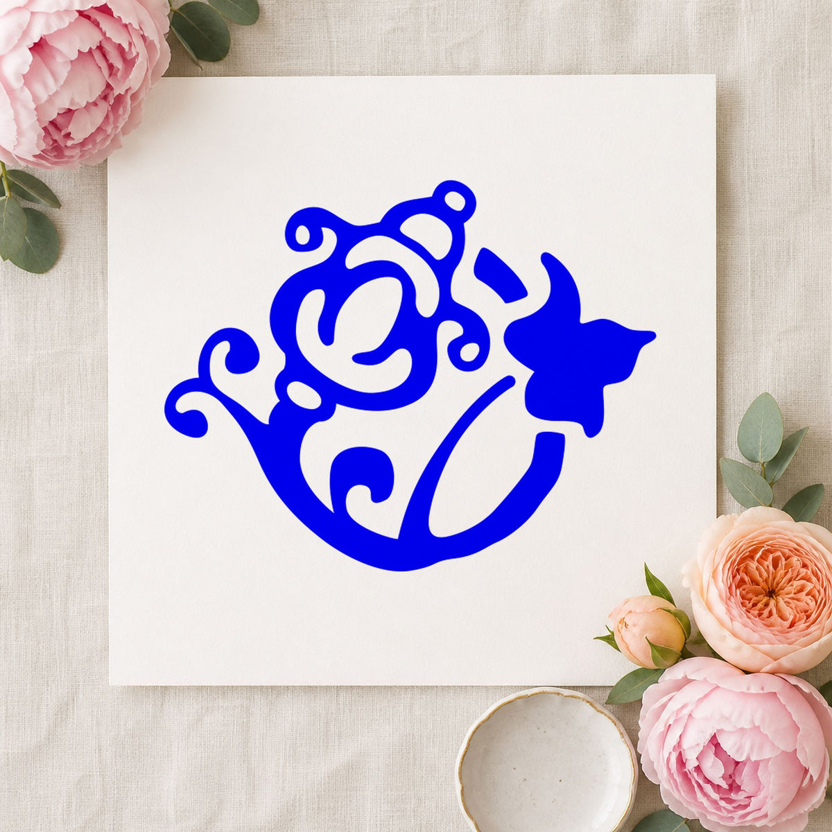 Flower and Watering Can Rubber Stamp impression in blue ink on white paper in a styled craft setting.