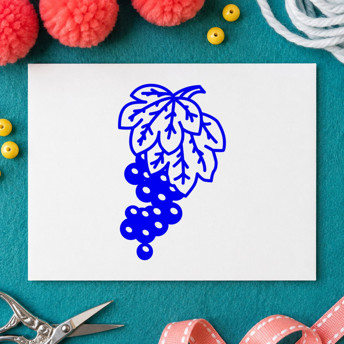 Blue fruit craft stamp impression featuring the grape bunch on vine design on white paper.