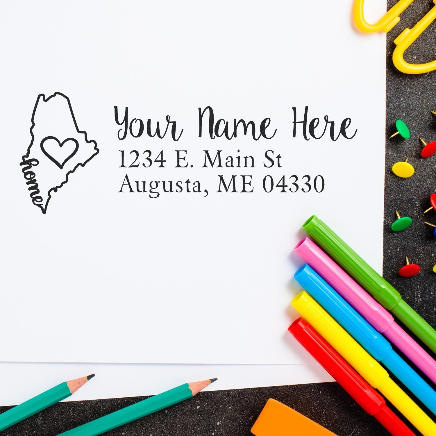 Custom Maine address rubber stamp with home icon and return address on paper, surrounded by colorful stationery.