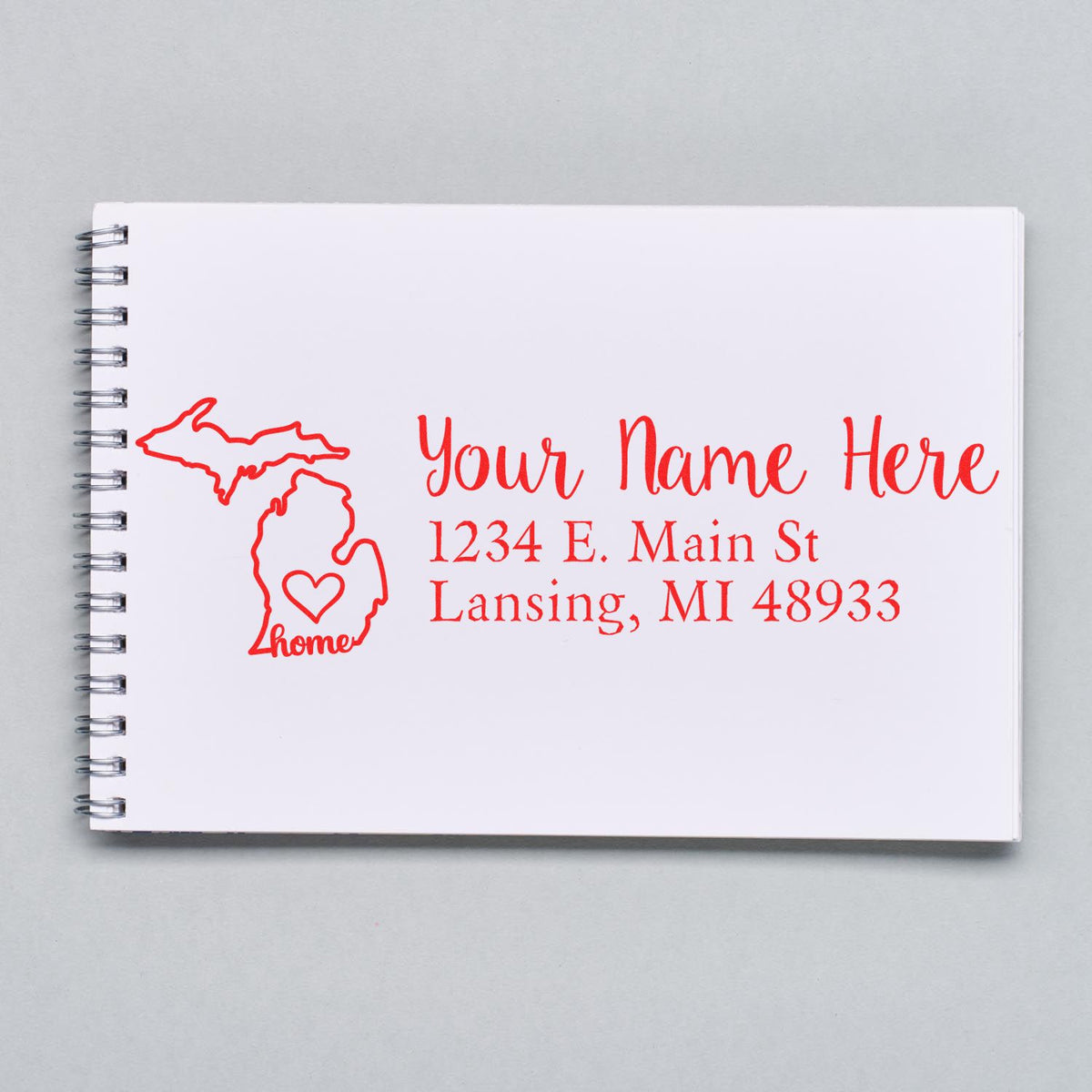 Custom Michigan home address rubber stamp with state outline, heart, and personalized name and return address on notebook.