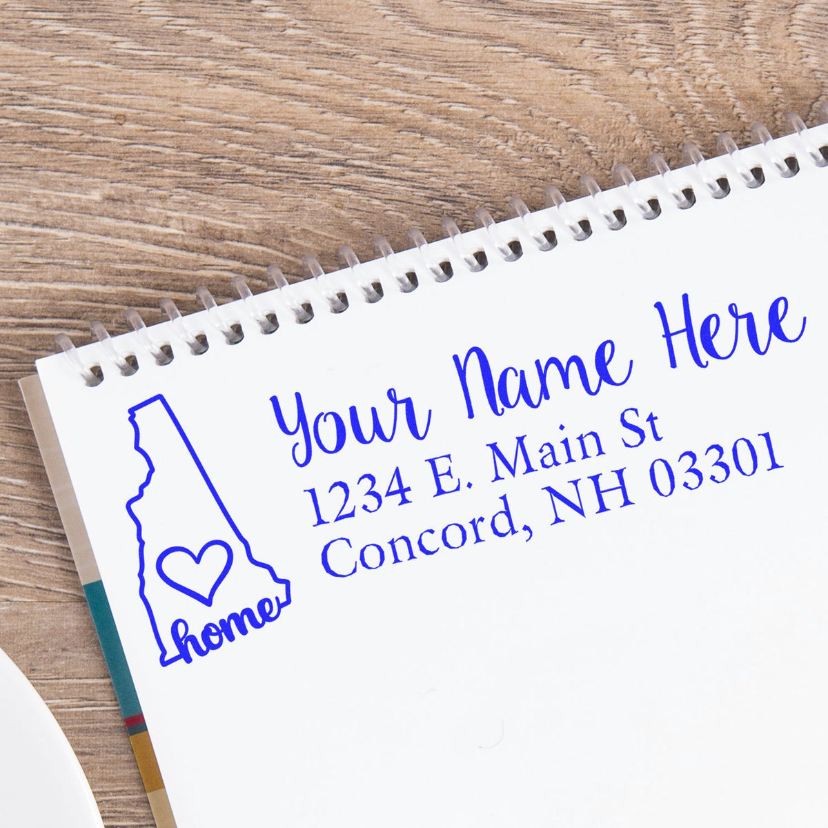 Custom return address rubber stamp with New Hampshire home design, personalized name, and mailing address on a notebook page.