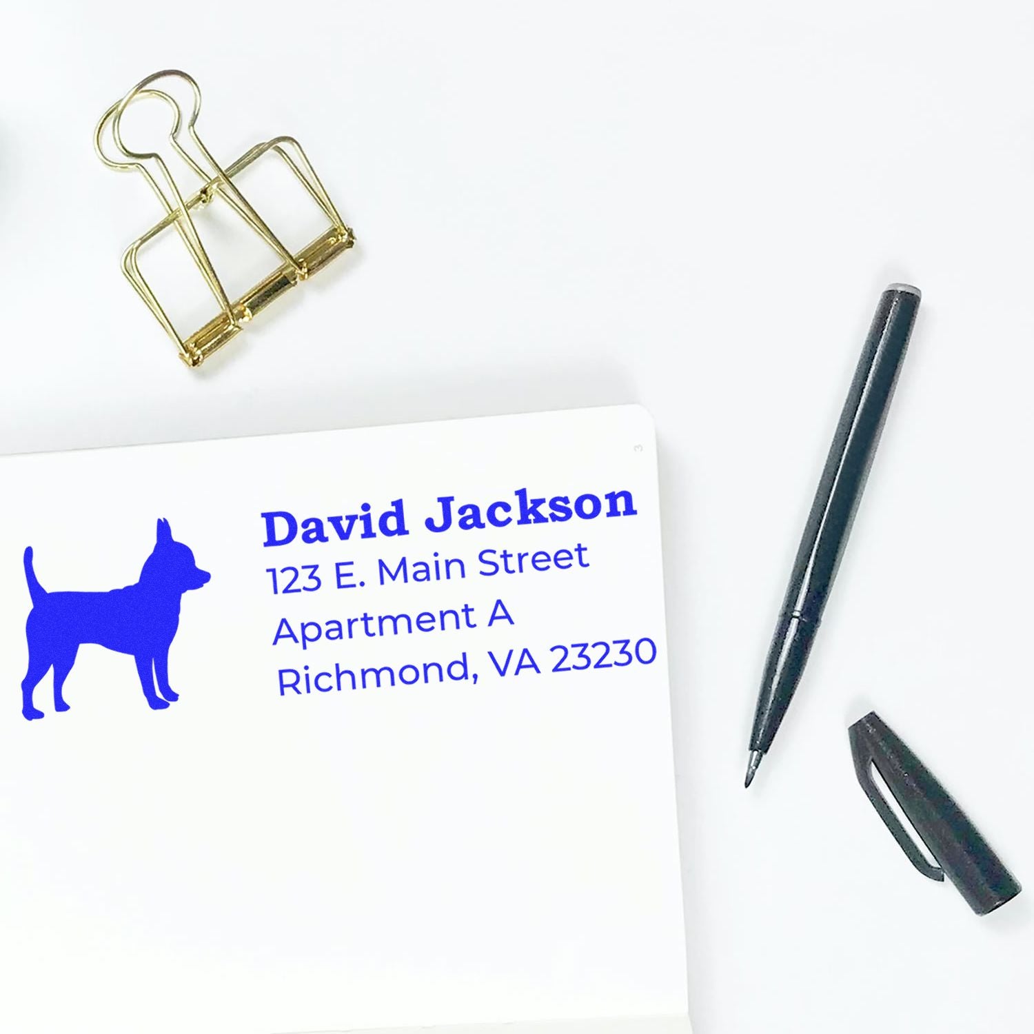 Custom address rubber stamp with dog silhouette, showing a blue personalized mailing imprint on paper.