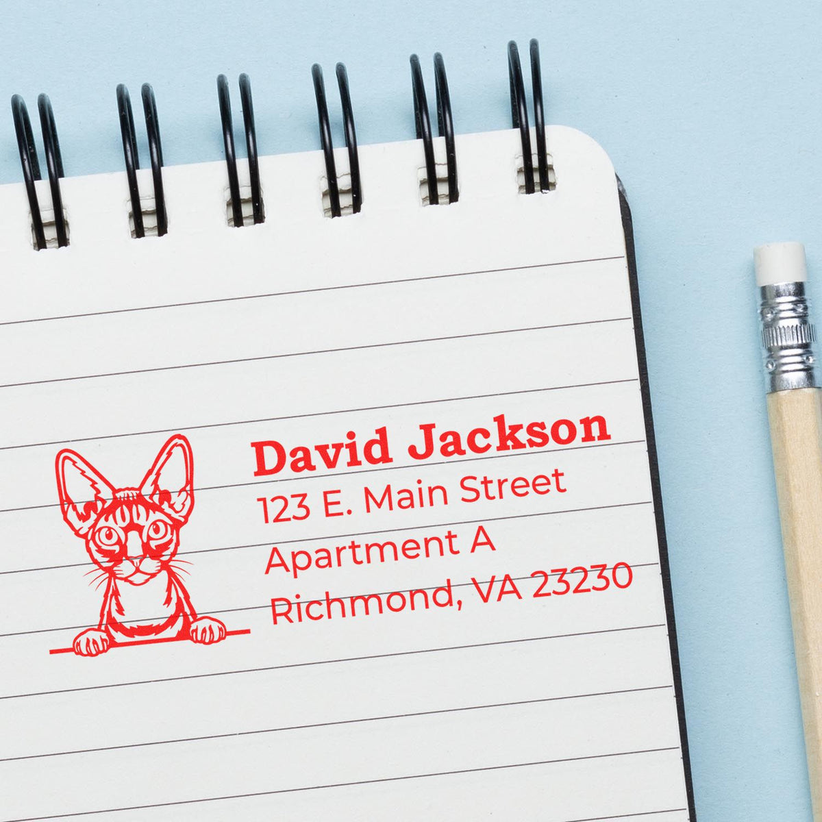 Personalized rubber address stamp with cat illustration, used to imprint name and mailing address on a notebook page.