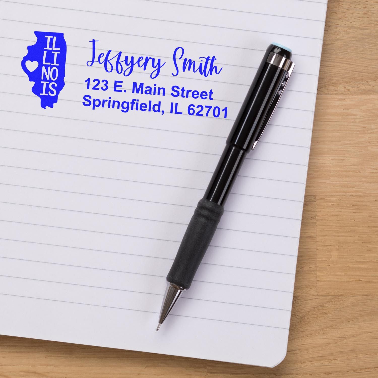 Personalized Illinois return address rubber stamp with name and address beside a pen on notebook paper