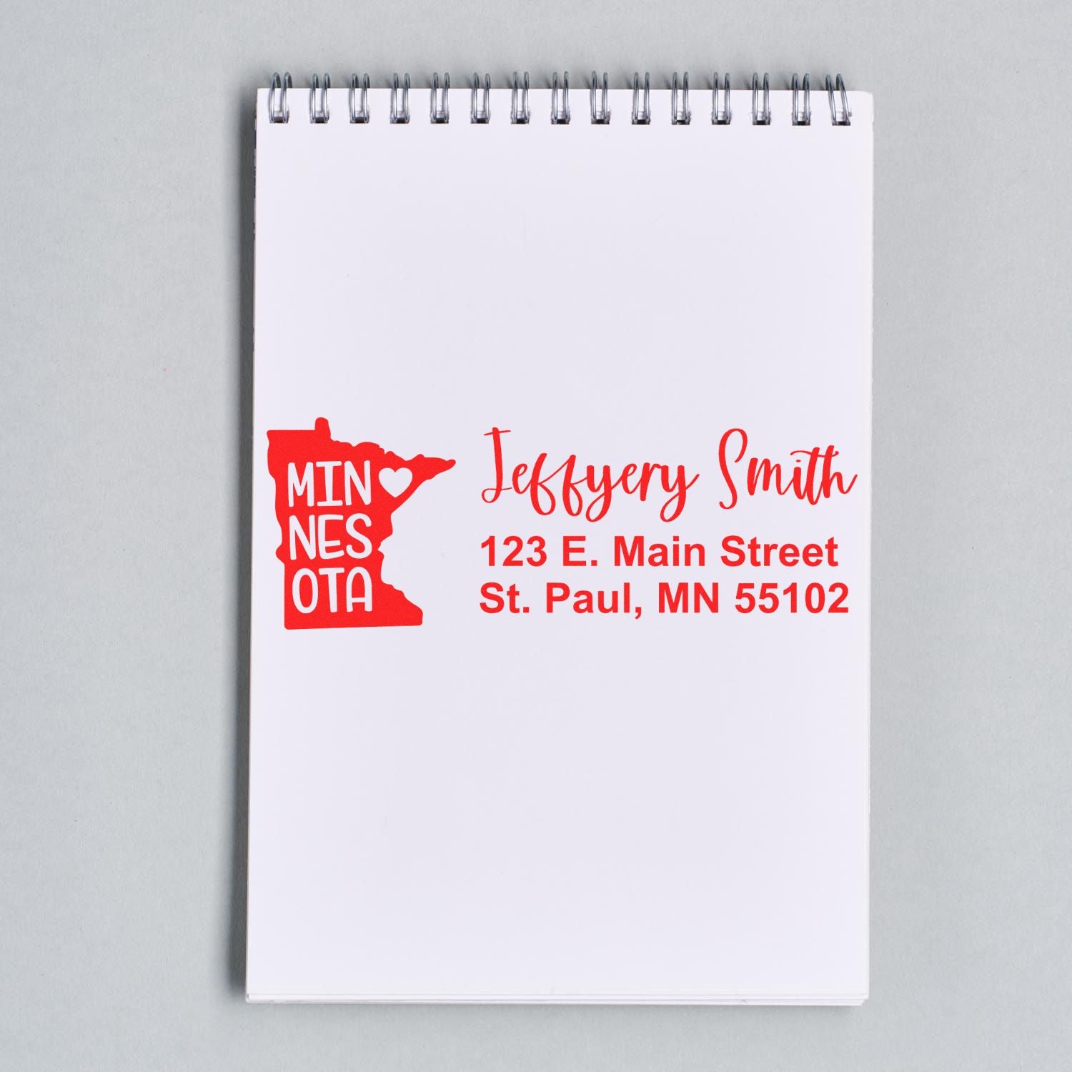 Red custom Minnesota return address rubber stamp imprint with name and St. Paul, MN address on a notebook page.