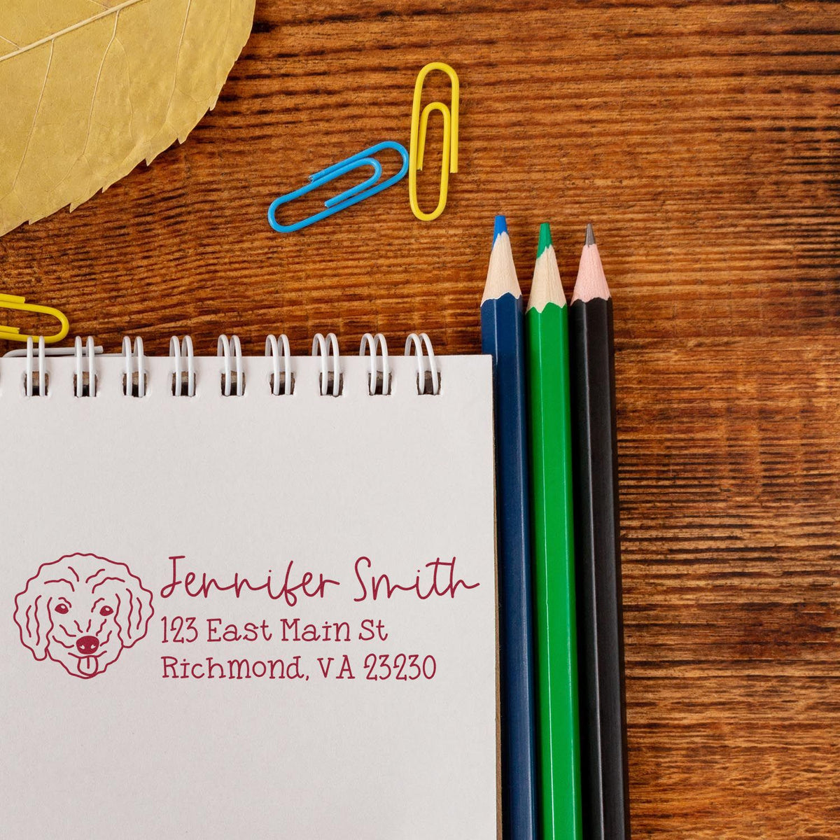 Custom return address rubber stamp with dog logo for Jennifer Smith, stamped on a notebook beside pencils.