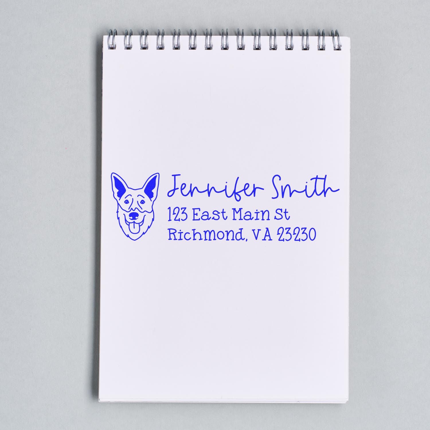 Custom rubber address stamp with dog logo, personalized name and address, printed in blue on notepad.