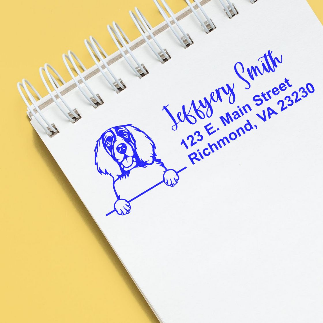 Custom rubber address stamp with dog illustration and personalized return address on a spiral notebook.