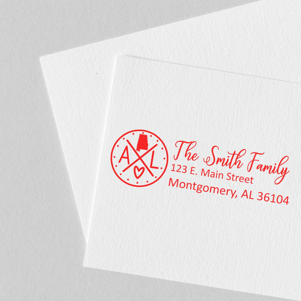 Custom family return address rubber stamp on white envelopes with red monogram and name, used for mailing and invitations.