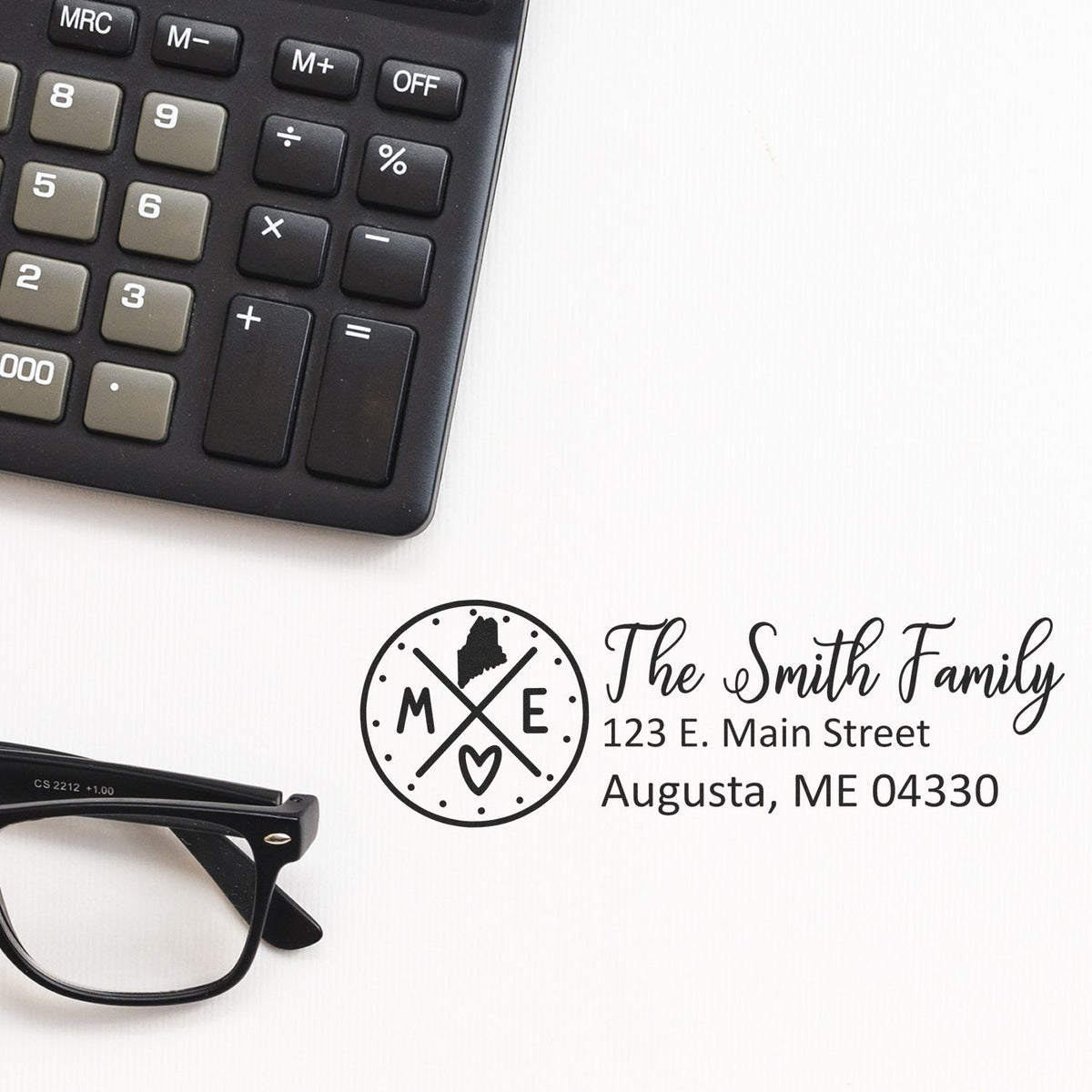 Custom return address rubber stamp with The Smith Family name and Augusta, ME address beside calculator and glasses.