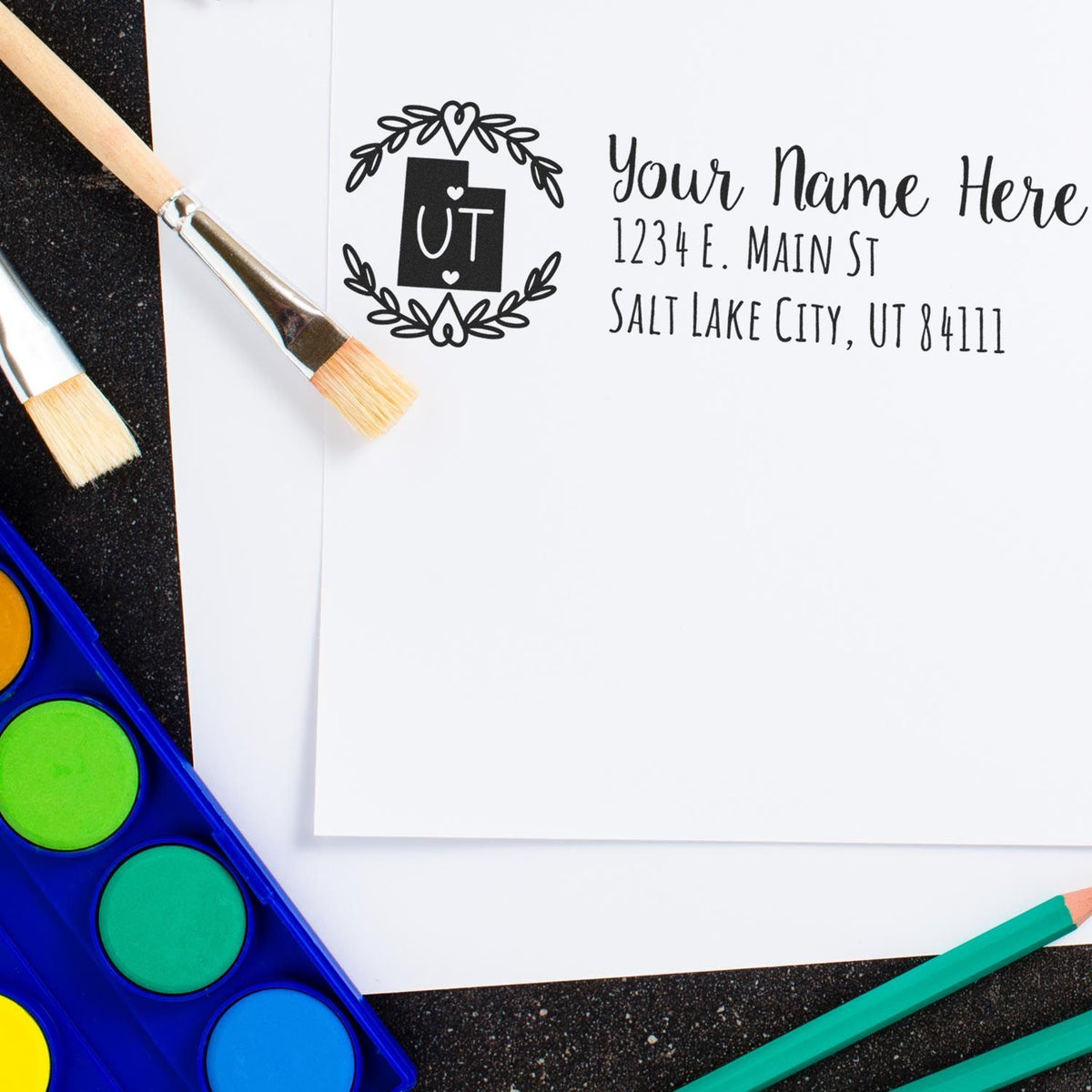 Custom return address rubber stamp with floral UT monogram, shown on paper with art supplies for personalized stationery.