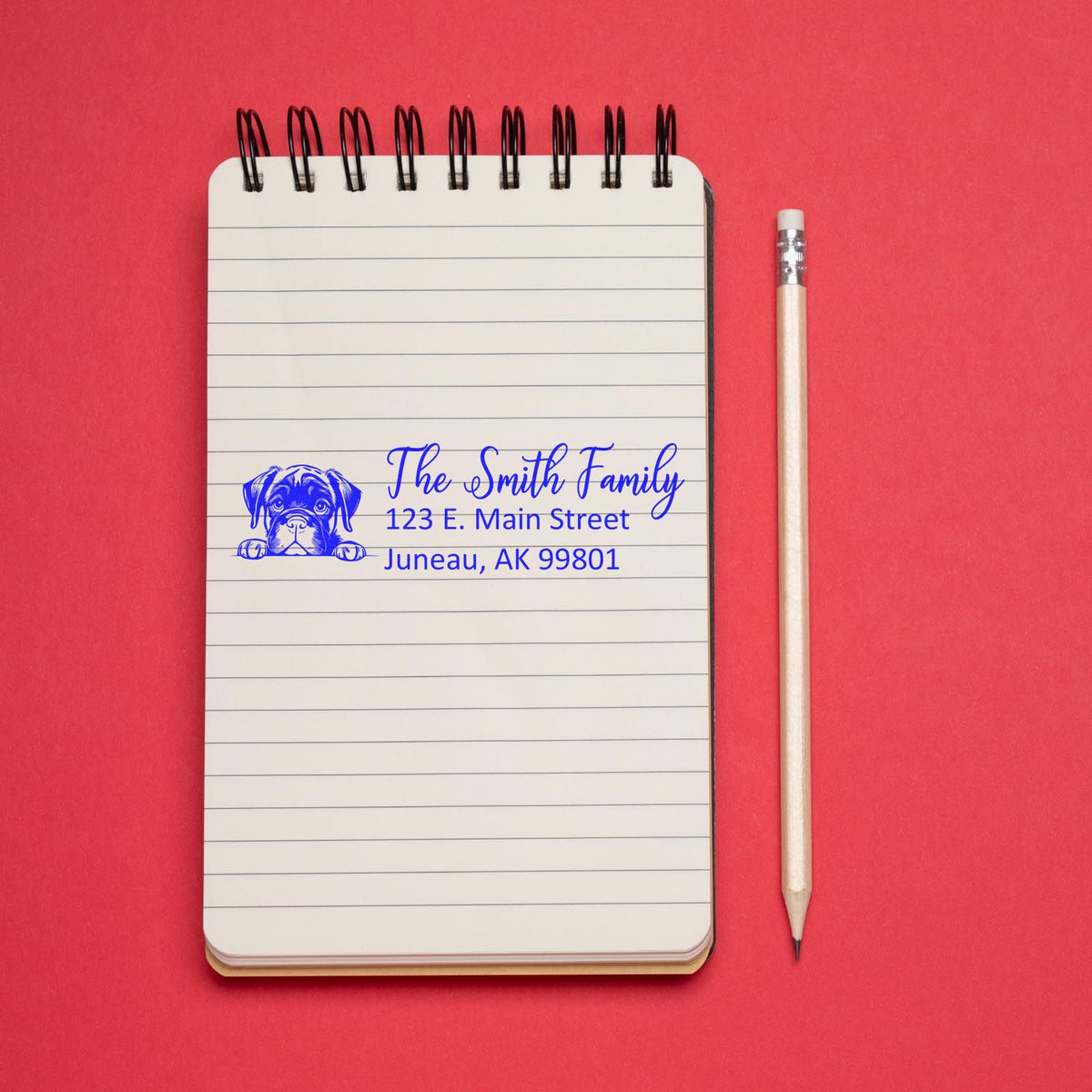 Custom dog address rubber stamp with family name and return address, shown on a notebook beside a pencil.