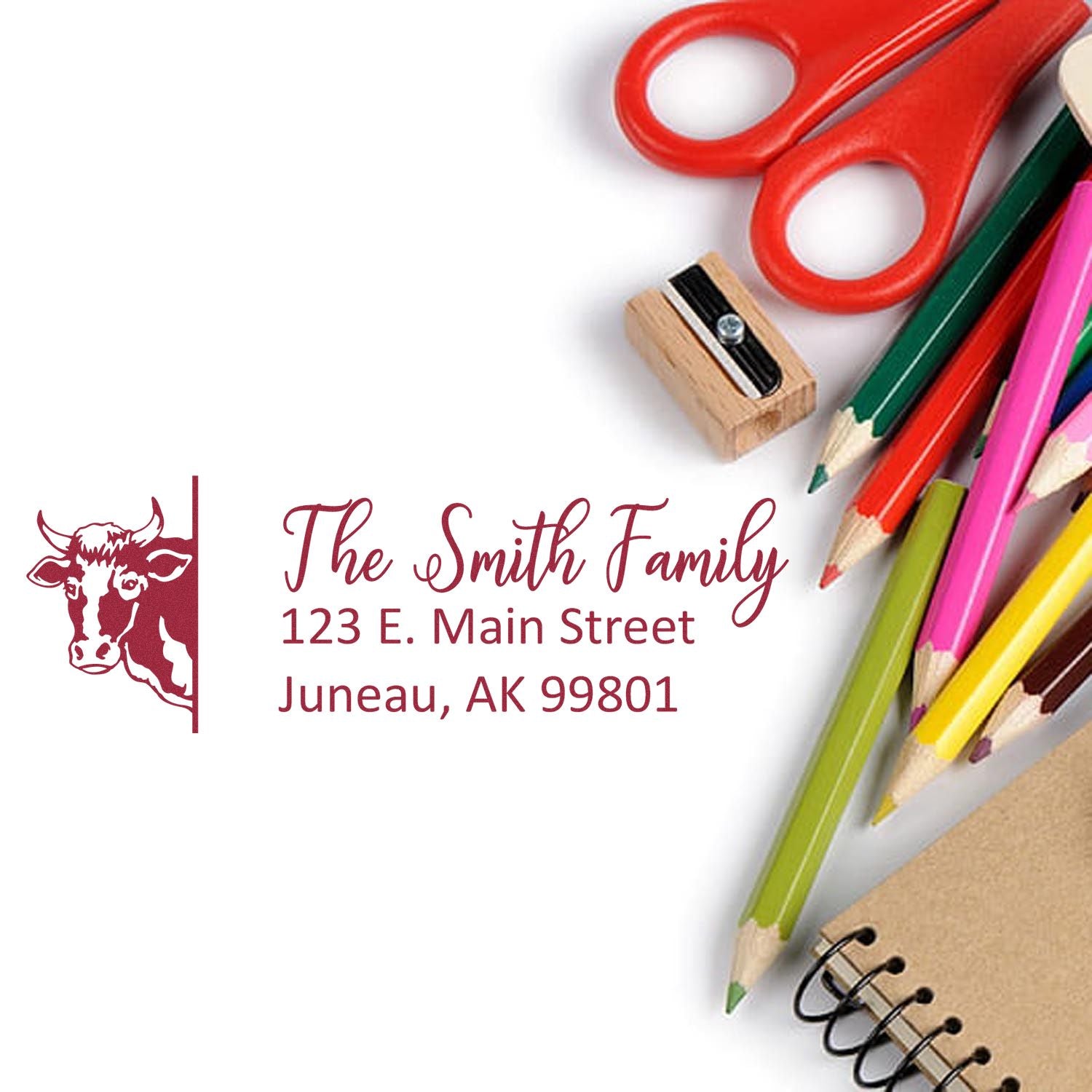 Custom family return address rubber stamp with cow design, The Smith Family, Juneau AK, shown with stationery and craft supplies.
