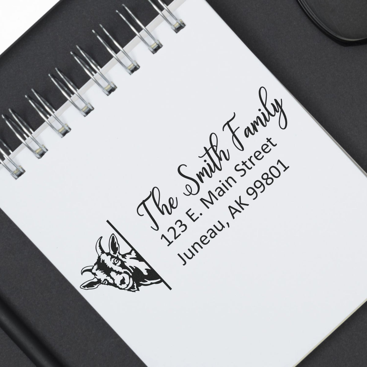 Custom return address rubber stamp for The Smith Family with horse logo, shown on a notebook cover.