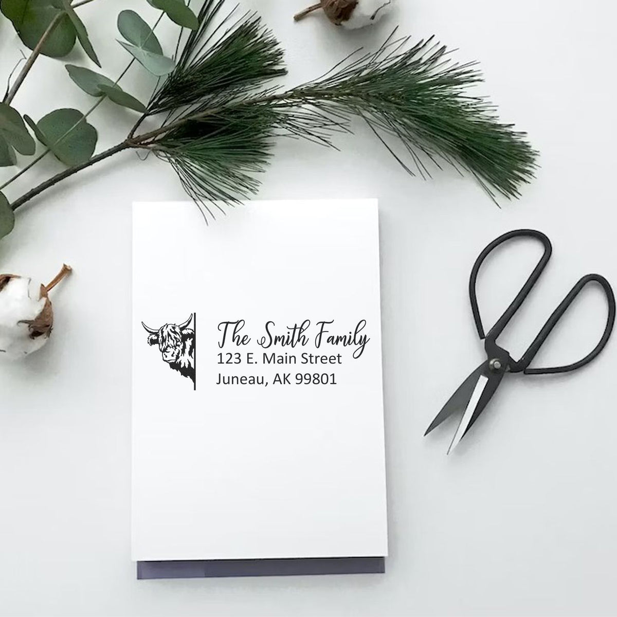 Custom return address rubber stamp with cow design on stationery, styled with greenery and scissors for personalized mailings.