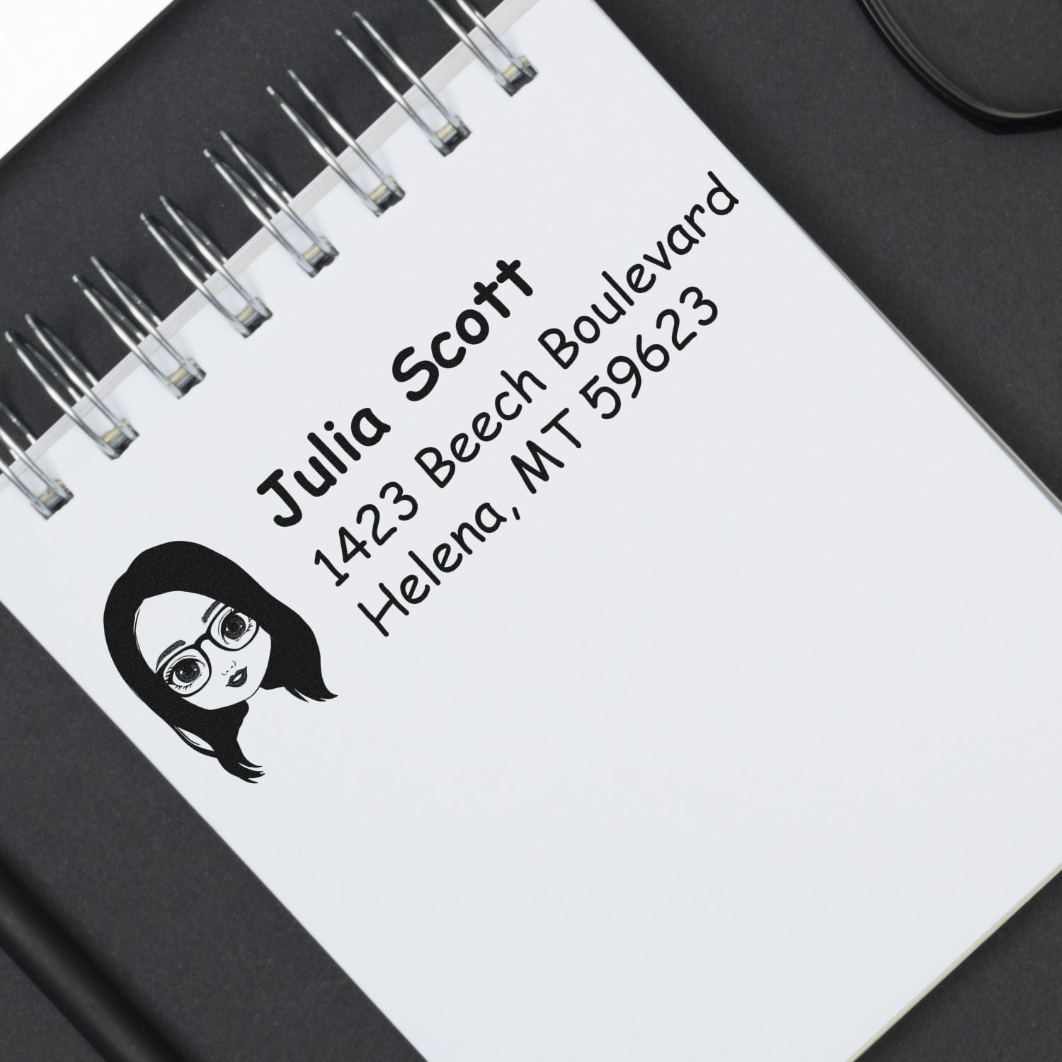 Custom return address rubber stamp with personalized name and address, shown on a notebook cover for mailing and packaging use.