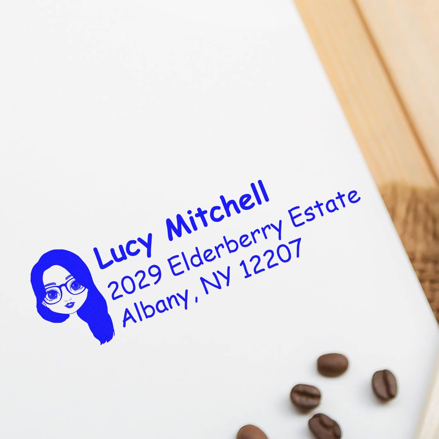 Custom rubber return address stamp for Lucy Mitchell on a white envelope, featuring blue name, address, and logo.