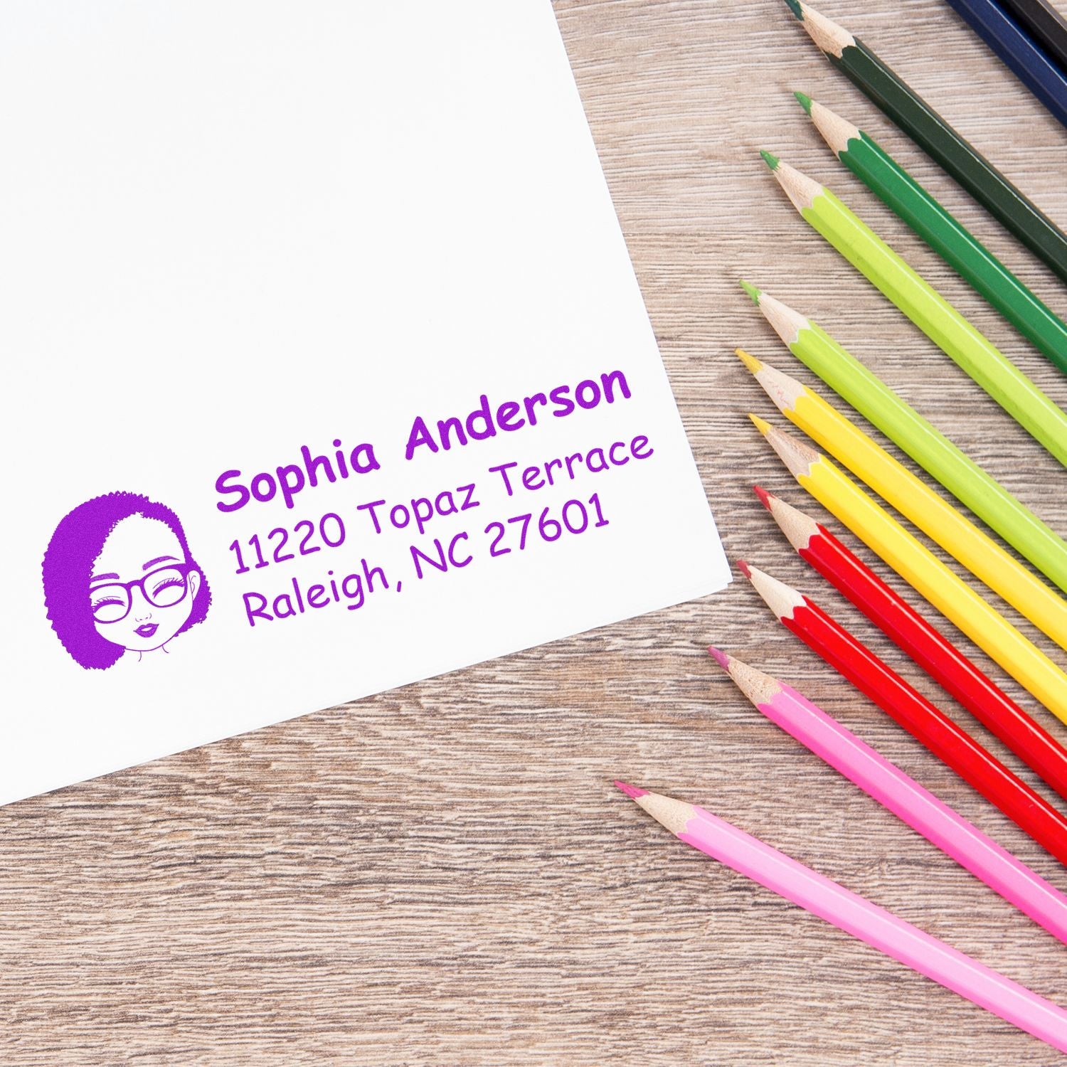 Custom address rubber stamp impression with name and address, shown on paper beside colored pencils.