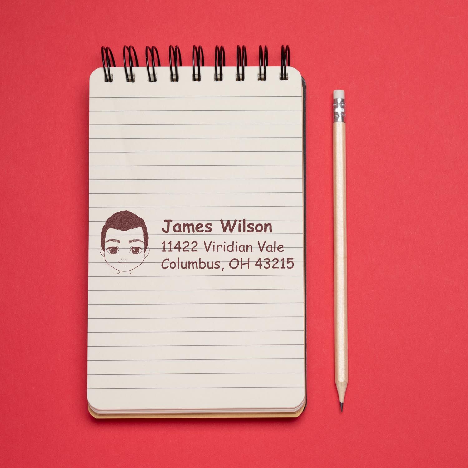 Custom rubber address stamp with cartoon portrait, name, and Columbus, OH return address stamped on a lined notebook.
