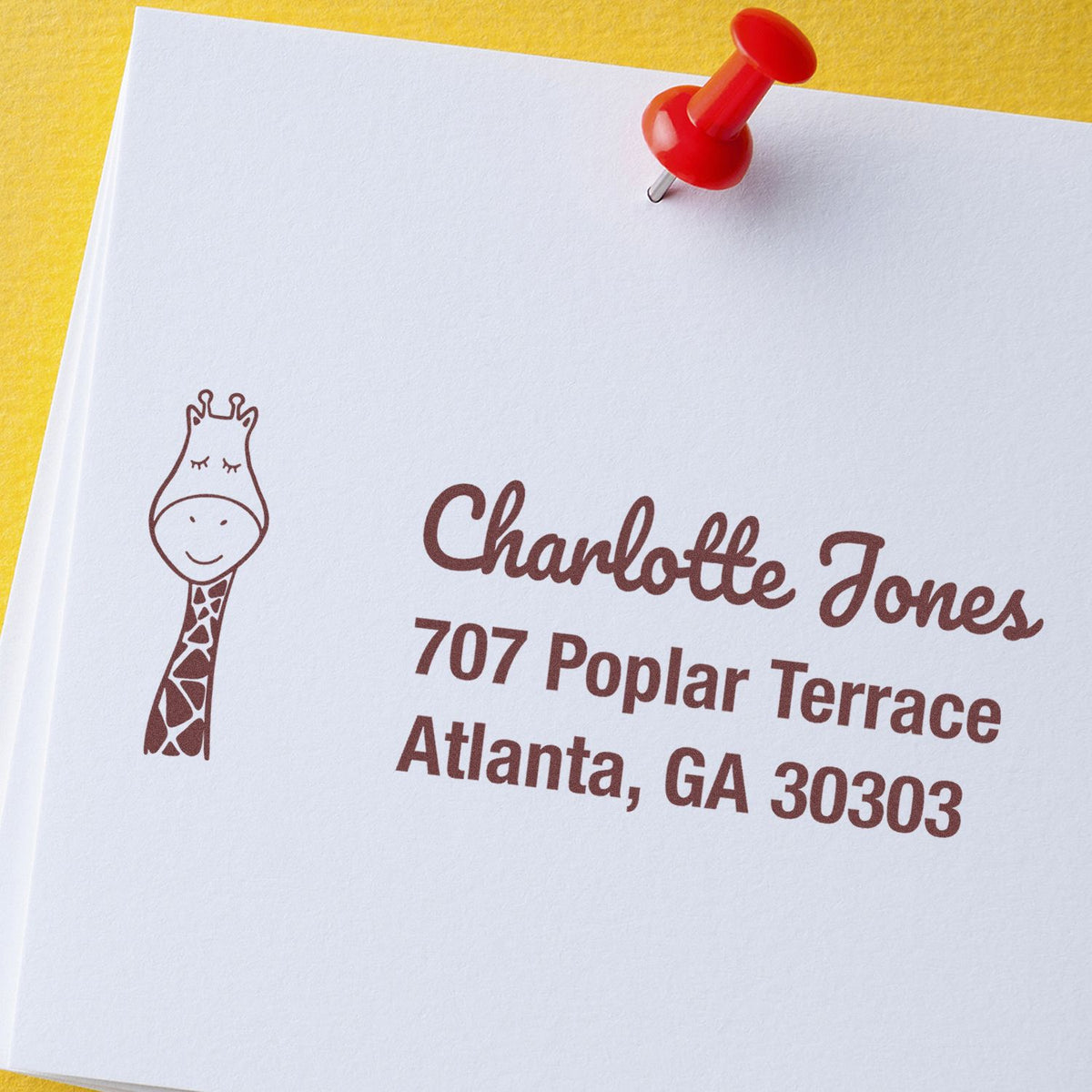 Custom rubber address stamp with giraffe logo for Charlotte Jones, Atlanta GA, on paper with red push pin.